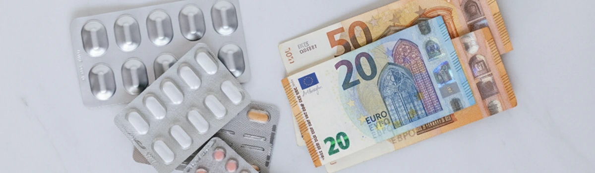 Blister packs of tablets next to 20 and 50 euro banknotes on a white surface